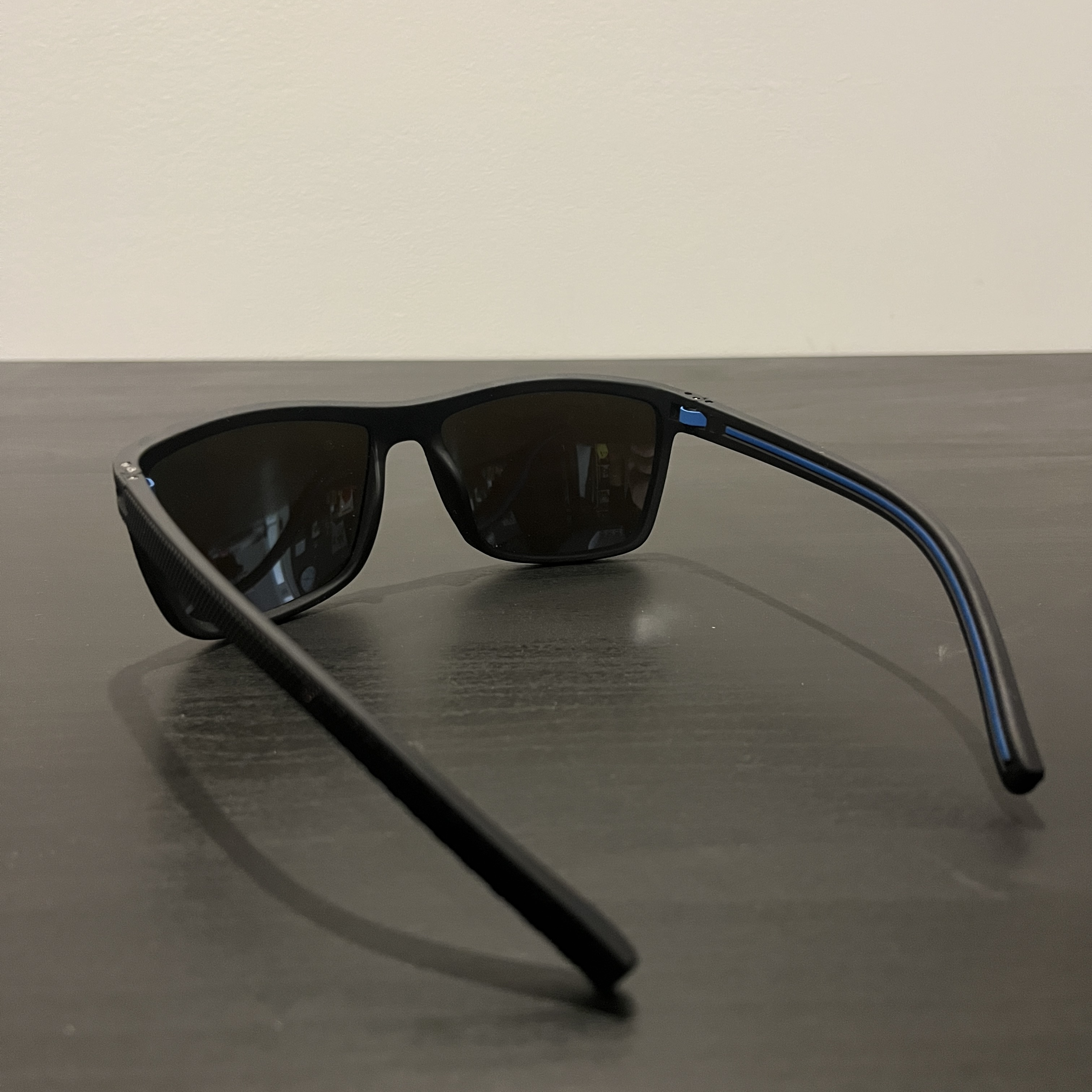 Black-rimmed sunglasses with blue lenses staged on a black table rear-left angle