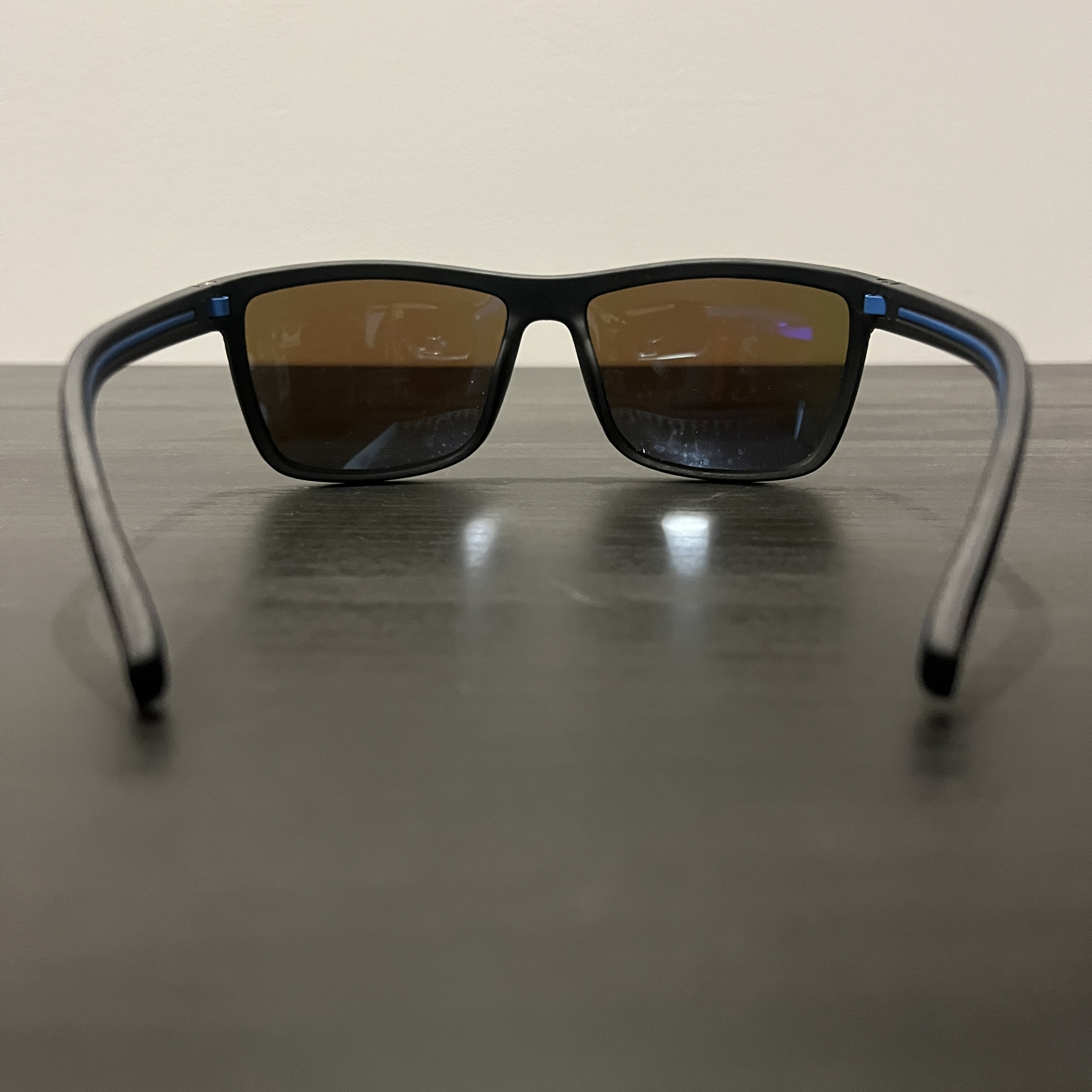 the back side of black-rimmed sunglasses with blue lenses staged on a black table.